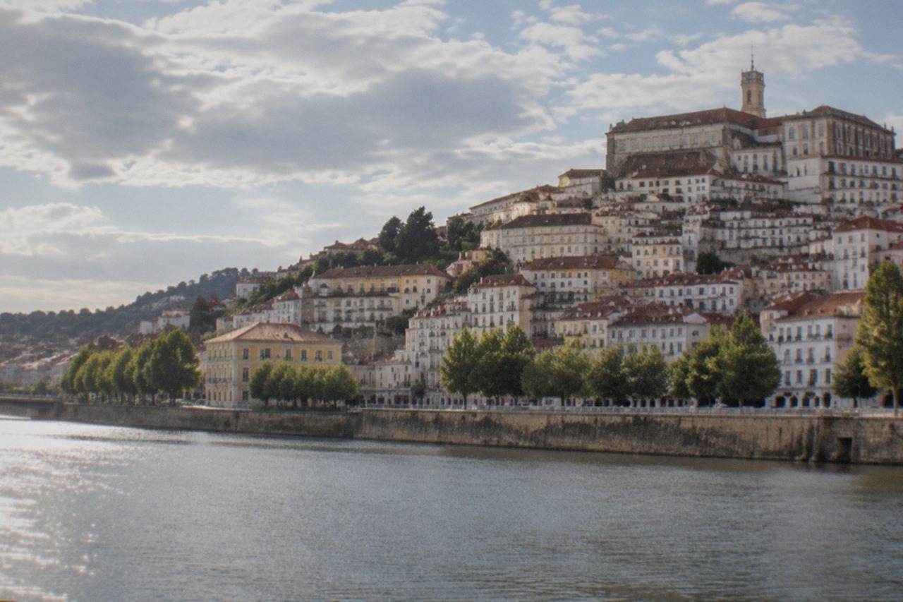 The hillside city of Coimbra in Portugal seen from across the River Mondego, with the university buildings rising above the old town rooftops