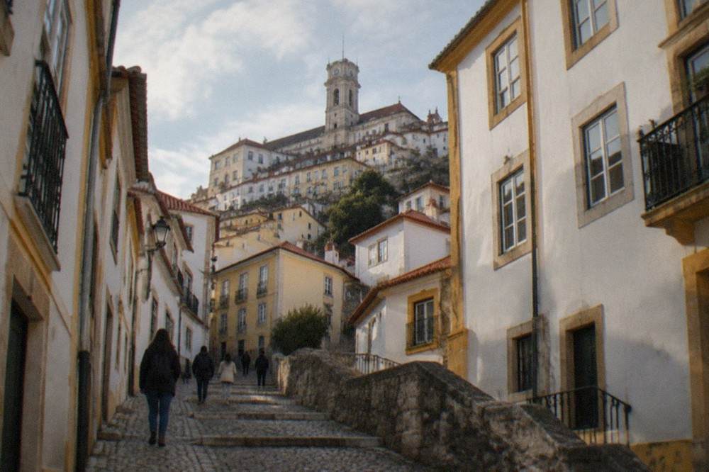 Visitors walking up a narrow cobbled street in Coimbra's old town toward the university hill on a bright afternoon