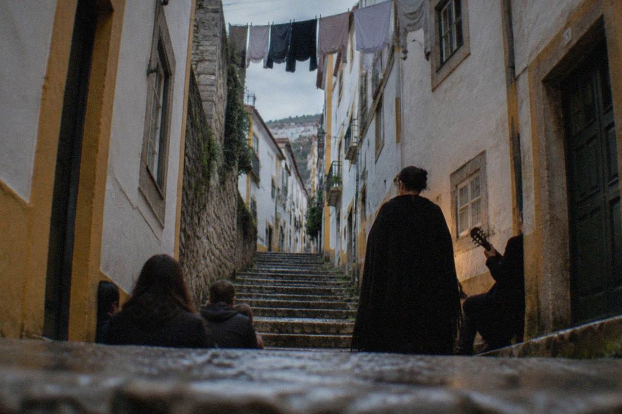 A singer in a dark academic cape performs fado in a dimly lit stone room in Coimbra