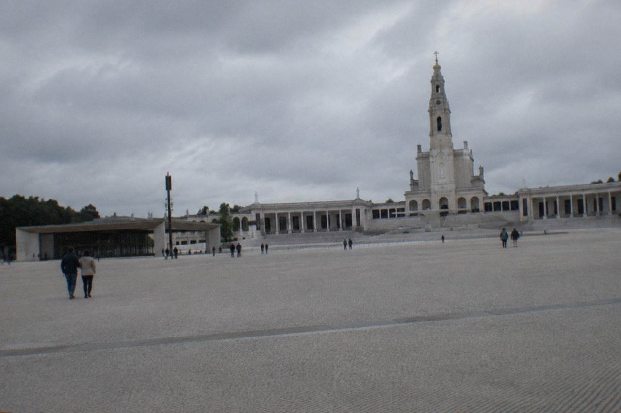 Pilgrims walking the broad esplanade in front of the Fátima sanctuary church under a bright sky