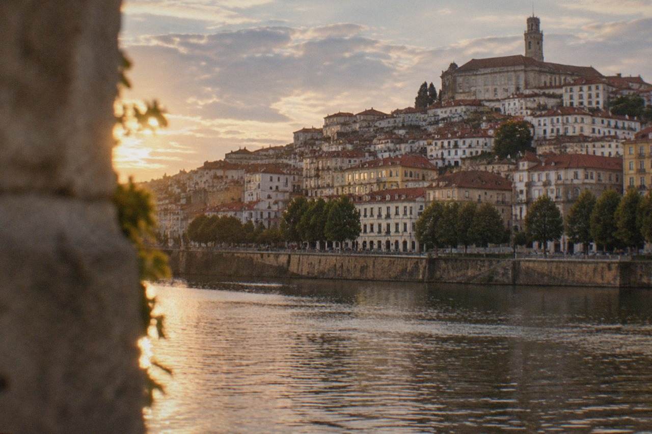 The old town of Coimbra in Portugal seen from across the River Mondego, with the university tower rising above terracotta rooftops.