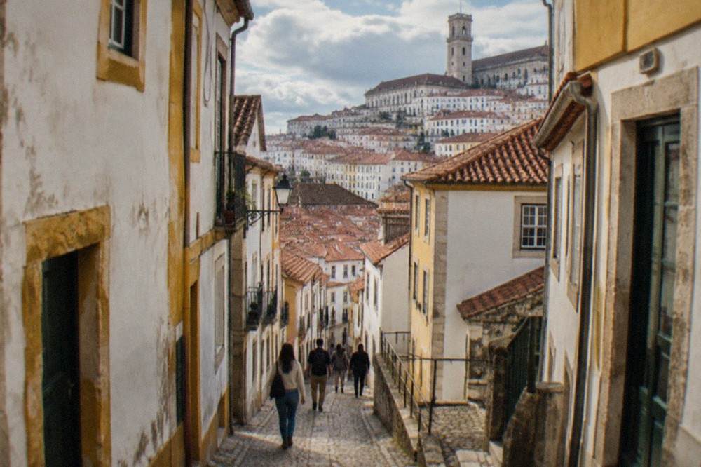 Visitors walking down a narrow cobbled lane between old buildings in Coimbra's old town