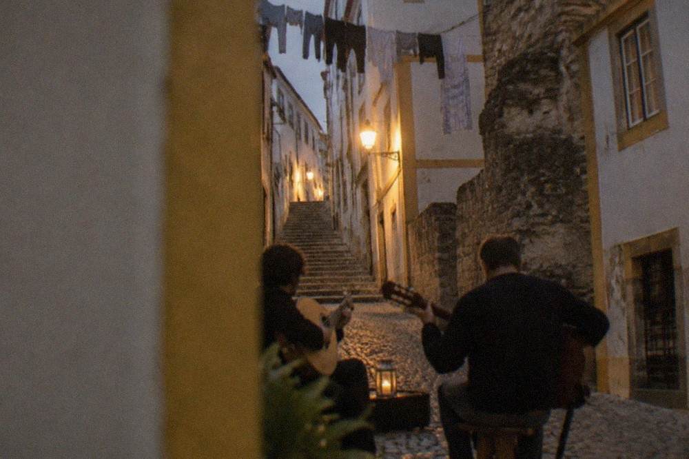 Two musicians playing the Portuguese guitar and classical guitar outdoors at night on a cobbled street in an old university town