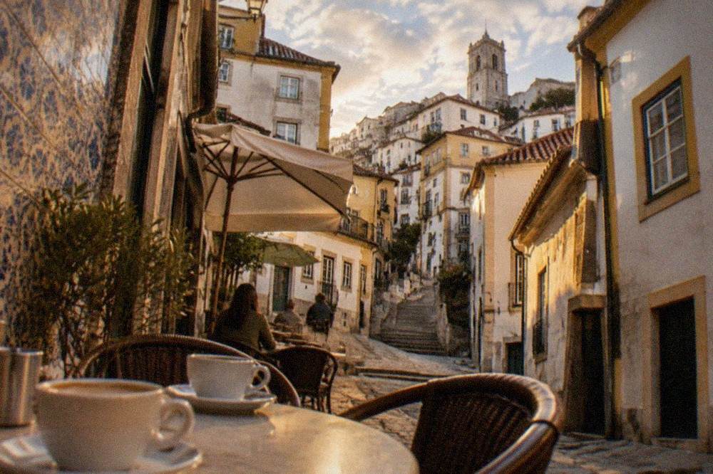 A café terrace in a narrow Coimbra street with tables, tiled walls and coffee cups