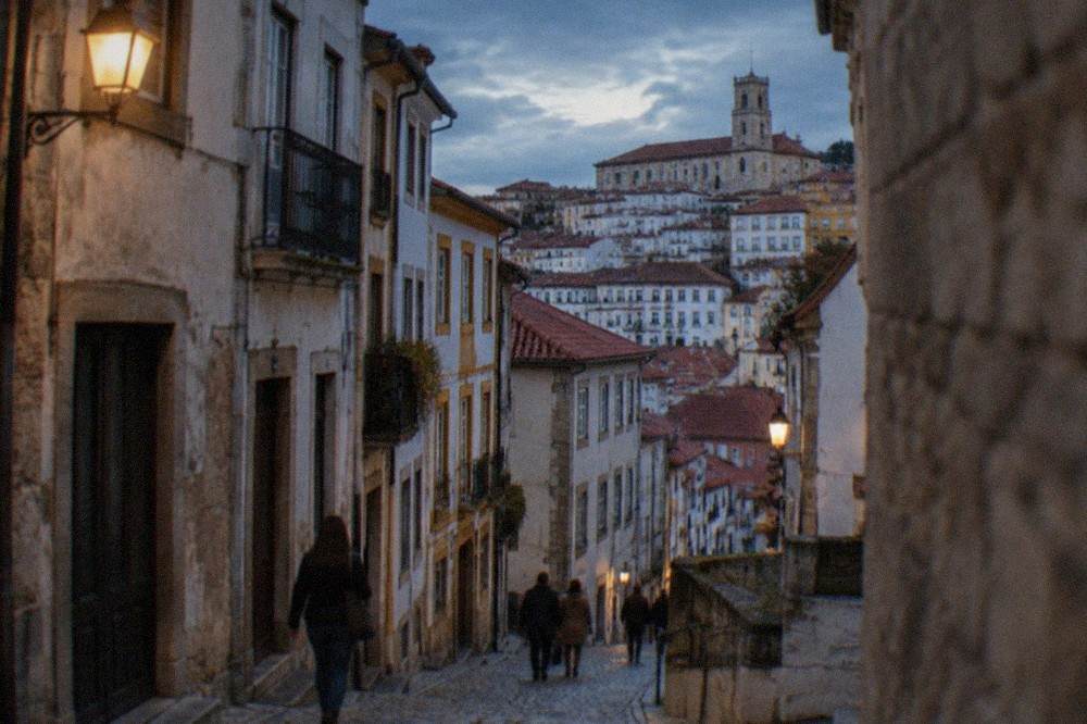 Visitors walking along a cobbled medieval street lined with old stone buildings in Coimbra's old town