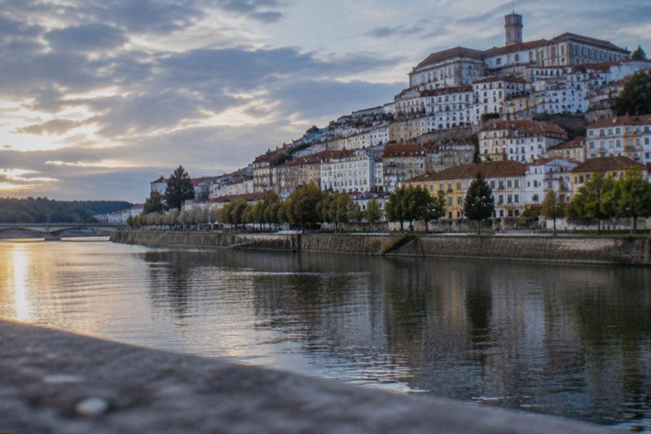 The historic university buildings of Coimbra seen from across the River Mondego on a bright day