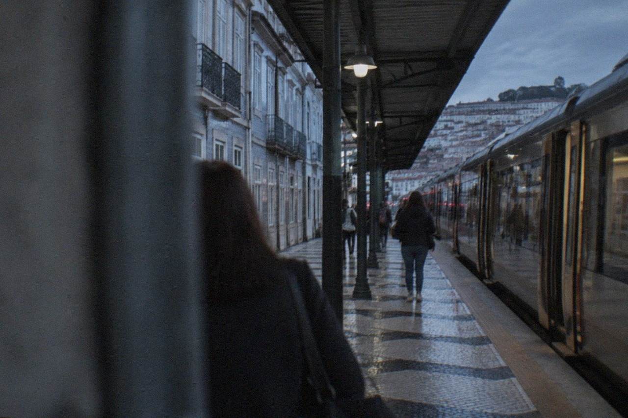 A railway platform in Coimbra with a passenger train stopped beside the covered walkway