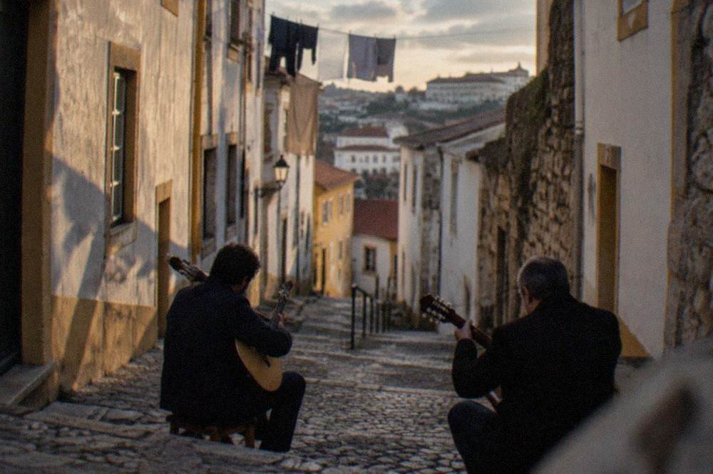 Two guitarists playing Portuguese guitars on a cobbled street in Coimbra's old town at dusk