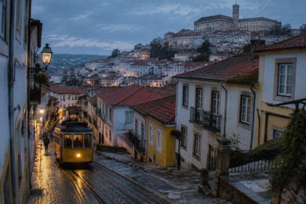 Wet cobbled street in Coimbra's old town with yellow tram and reflections after rain