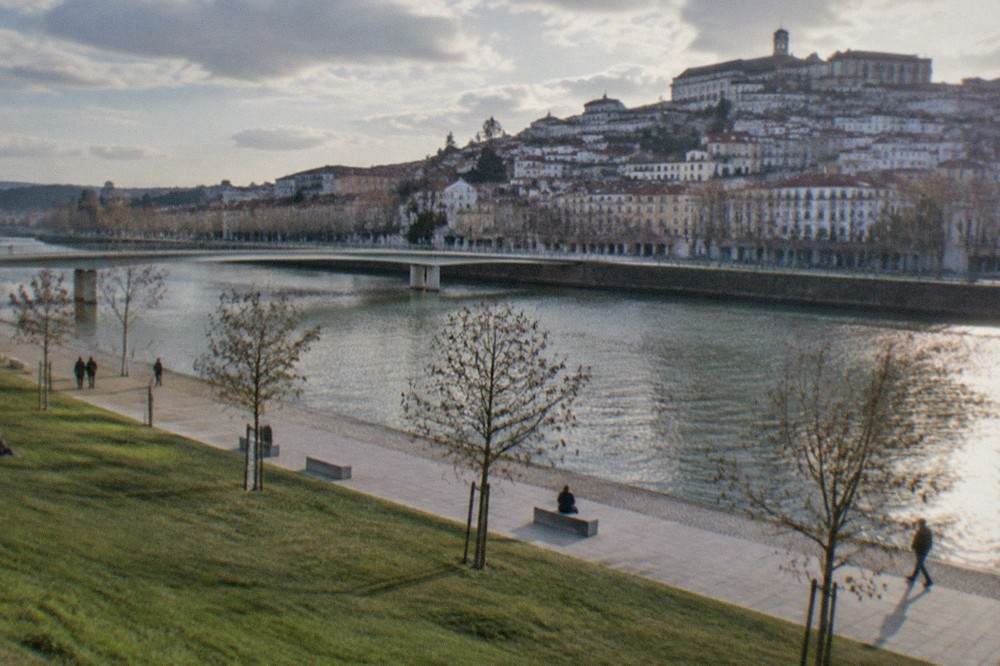 Riverside parkland beside the River Mondego in Coimbra, with the old town and university buildings on the far bank