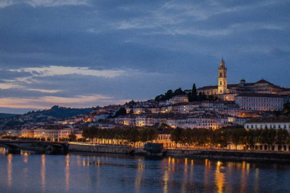 A night view over the illuminated old town of Coimbra with the university tower lit above the River Mondego