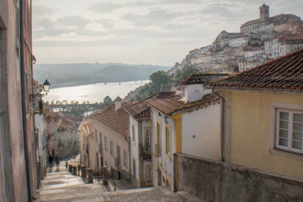 A quiet street in central Coimbra with pastel-coloured buildings and the river visible in the distance