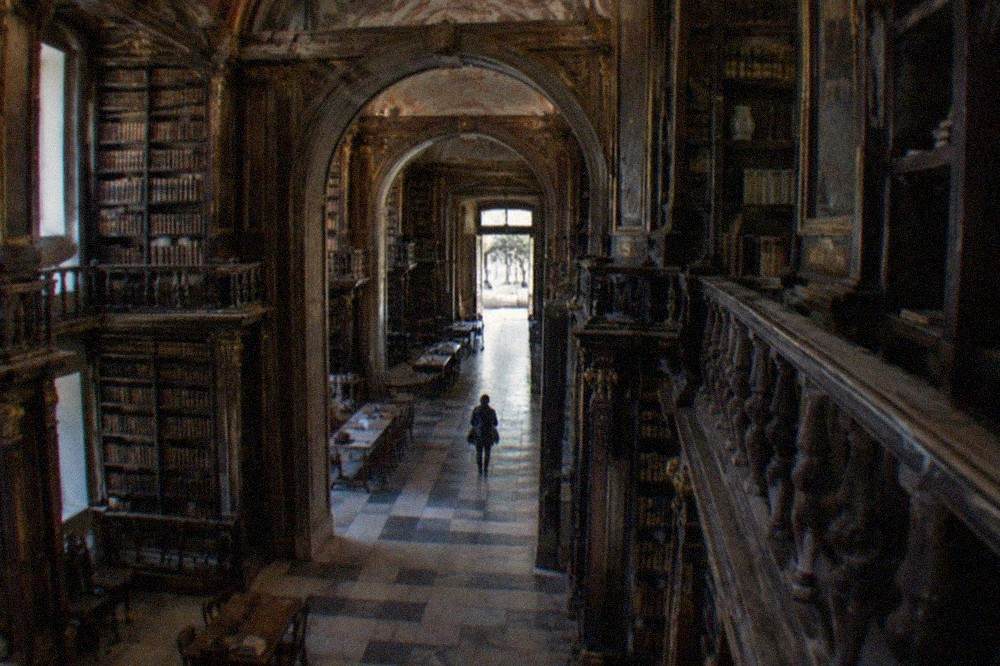 A visitor walking through an arched stone passage toward the entrance of a historic library building