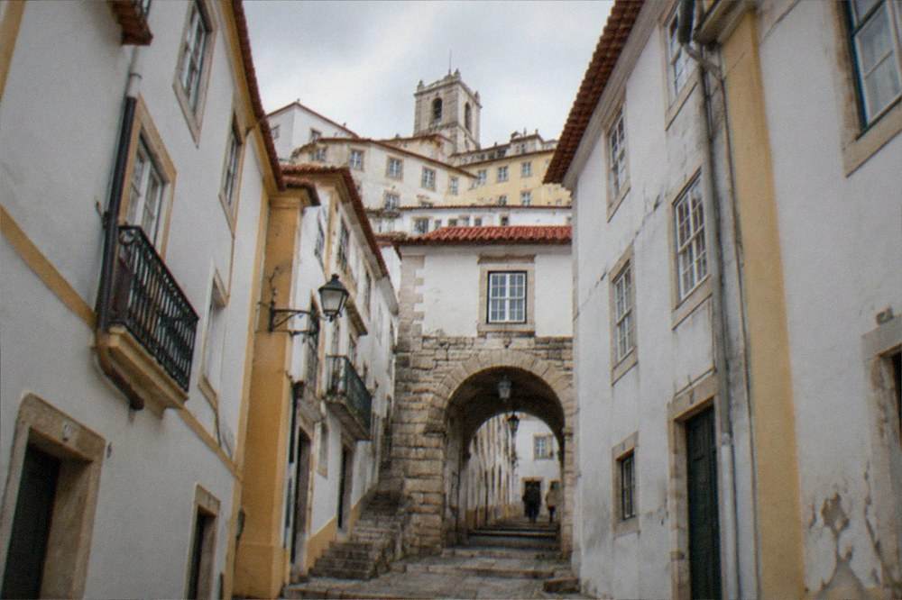 A stone arched gateway in a narrow street of old Coimbra with buildings rising above it