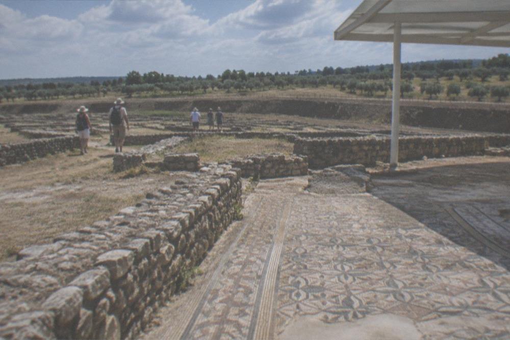 Visitors in sun hats walking between excavated stone walls on a warm day