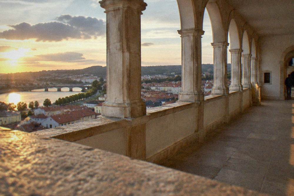A stone loggia with arched openings overlooking rooftops of a city and a river below