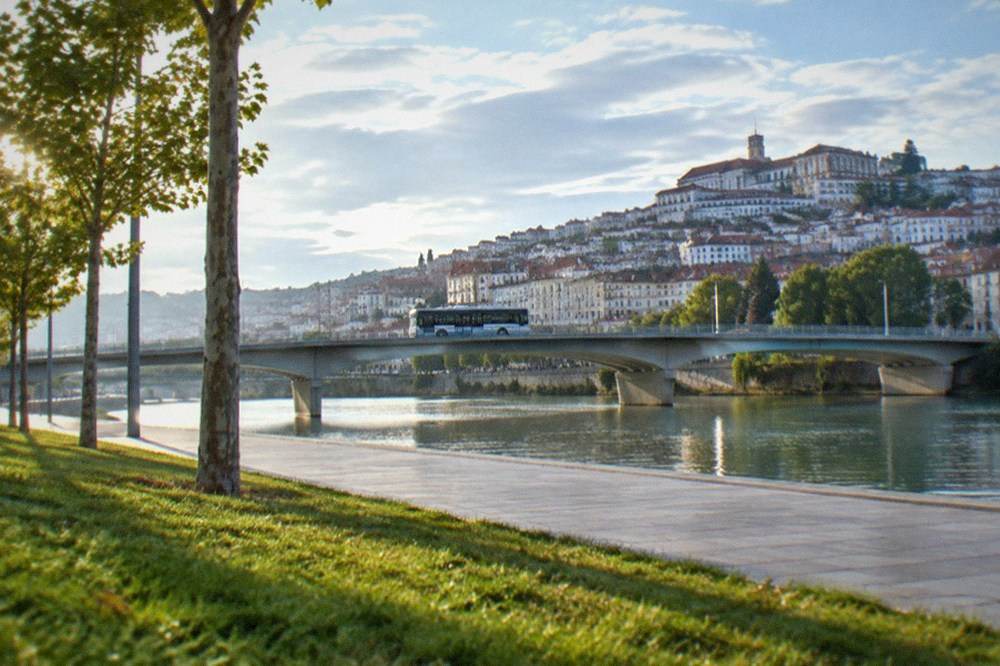 A city bus crossing a bridge over the River Mondego with the old town of Coimbra behind it