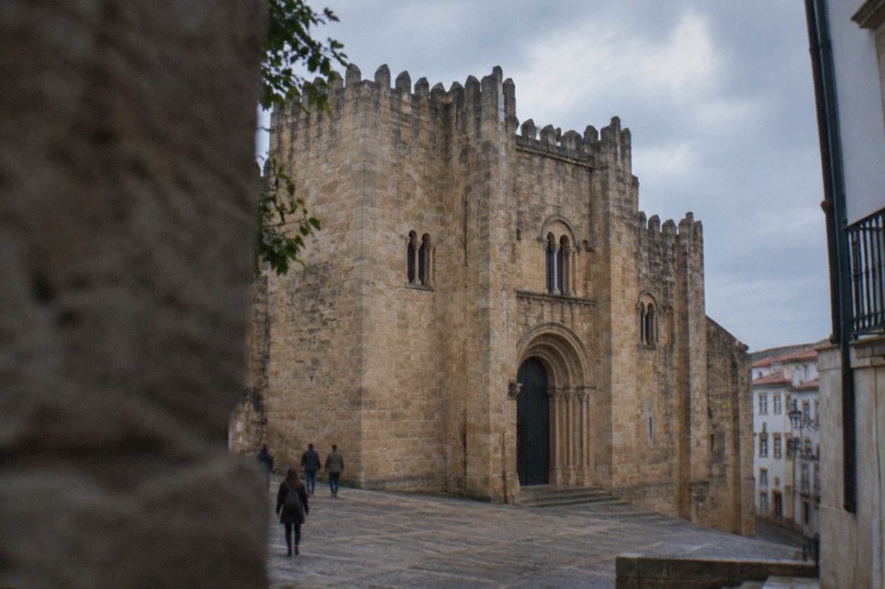 The fortified stone exterior of the Sé Velha old cathedral in Coimbra seen from the small square in front of it