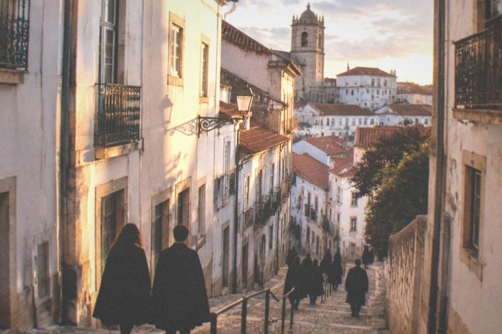 Students in traditional black capa e batina gowns walking through the old university buildings