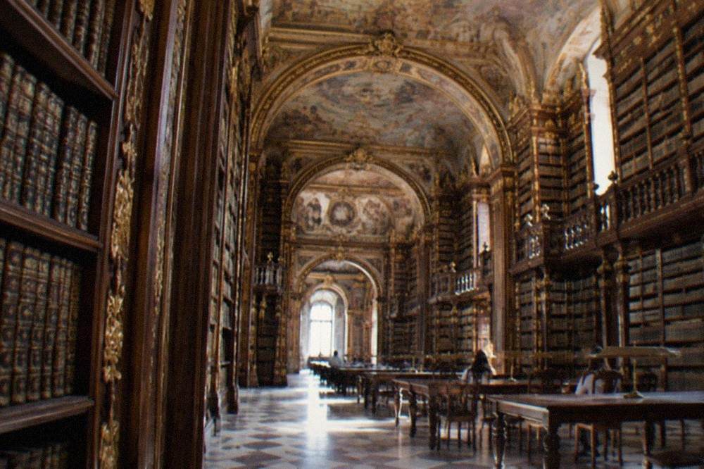 The ornate interior of the Biblioteca Joanina with tall gilded bookshelves and painted ceilings