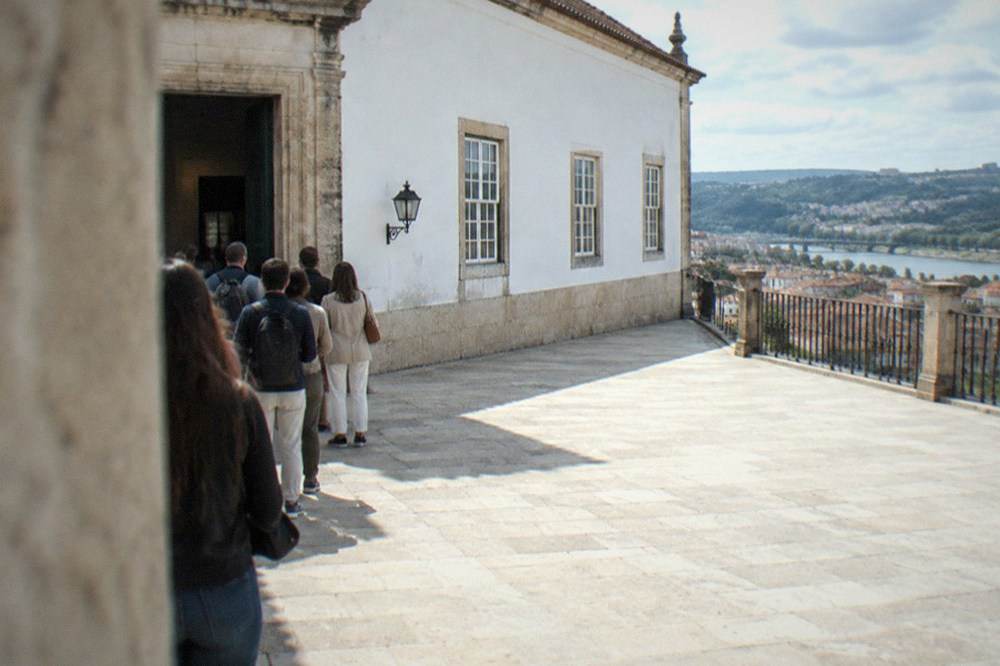 Visitors waiting at an old stone doorway inside the University of Coimbra before a timed library entry