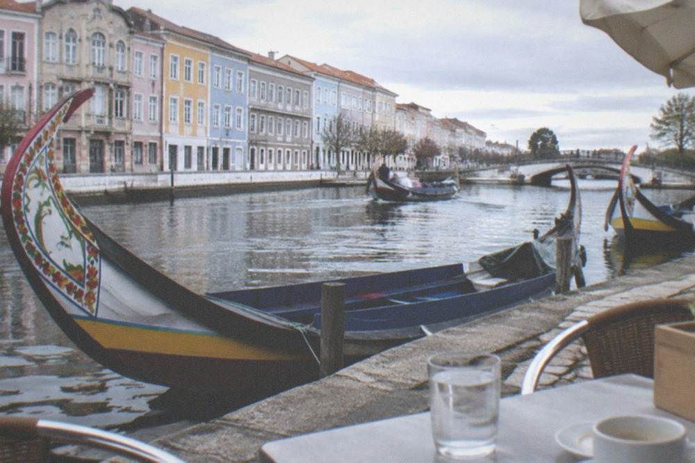 An outdoor cafe table beside an Aveiro canal with boats passing in the background