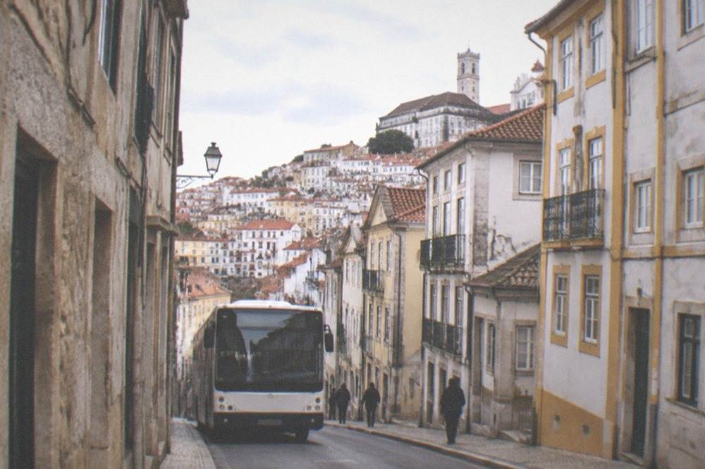 A city bus on a Coimbra street with the old town's stone buildings on either side