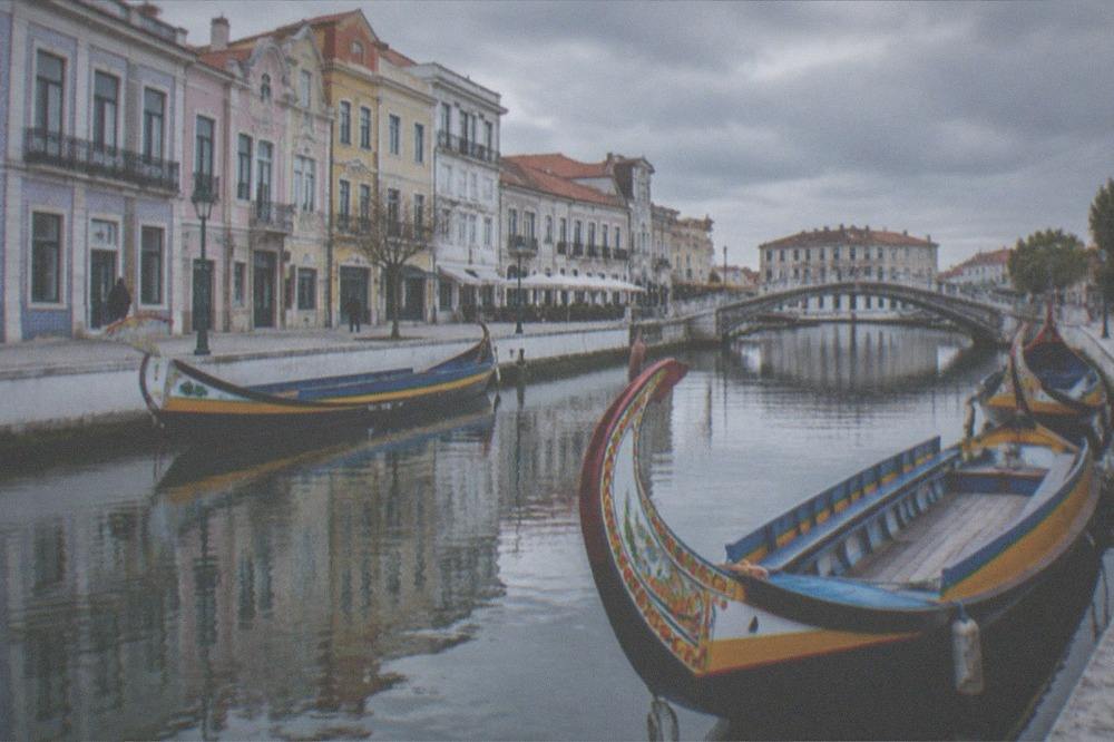 Colourful moliceiro boats moored on an Aveiro canal with boats and arched bridges reflected in the water