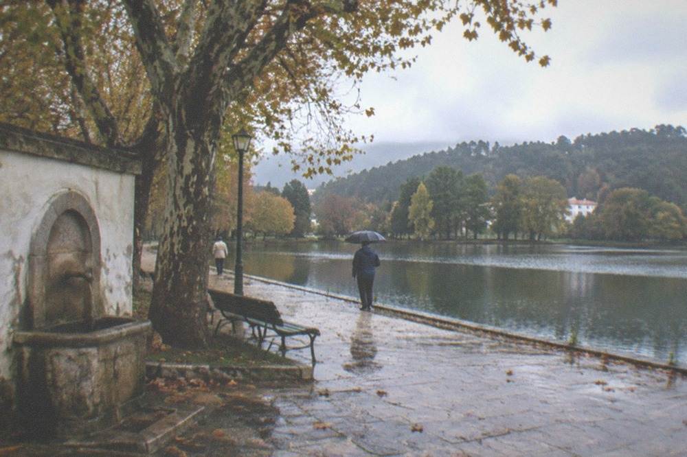 A lake with tree-lined banks in a Portuguese park under a cloudy autumn sky