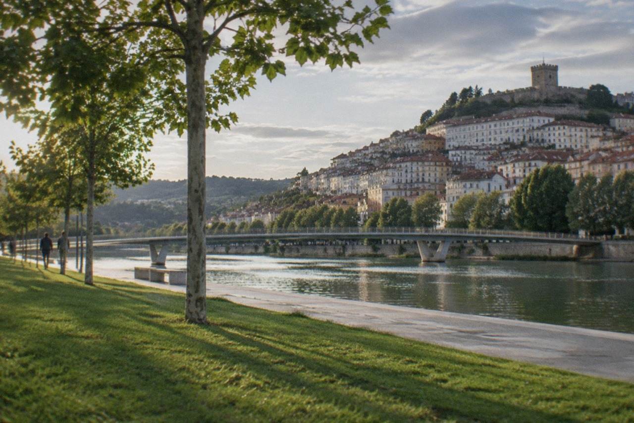 A stone castle keep rising above a walled town with the green Mondego valley beyond