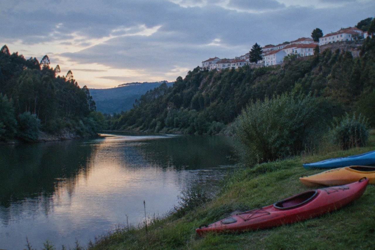 Kayaks resting on a grassy riverbank beside calm water with forested hills behind