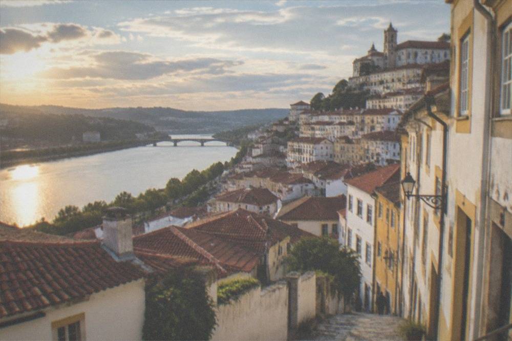 View over Coimbra rooftops toward the River Mondego in warm late afternoon light
