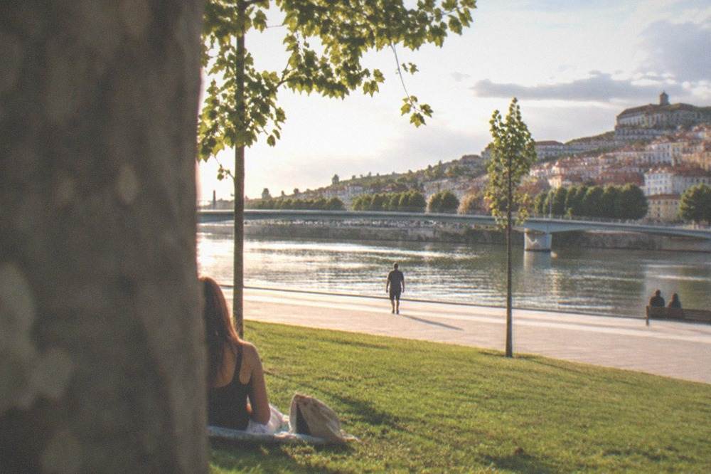 The Mondego riverside promenade in Coimbra in warm late afternoon light with few people about