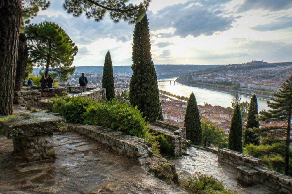 Visitors on a wide stone terrace looking out over a riverside city