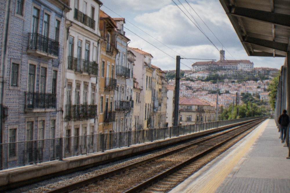 View along train tracks from a station platform with the city rooftops of Coimbra in the background