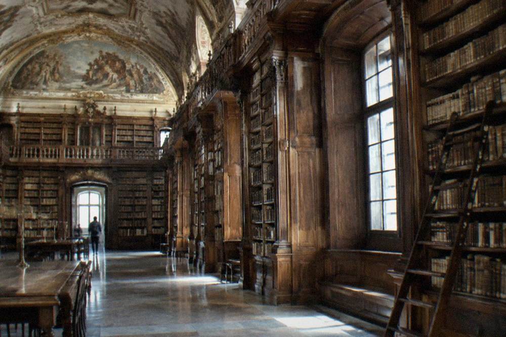 The baroque interior of a library hall with tall wooden bookshelves and painted ceilings