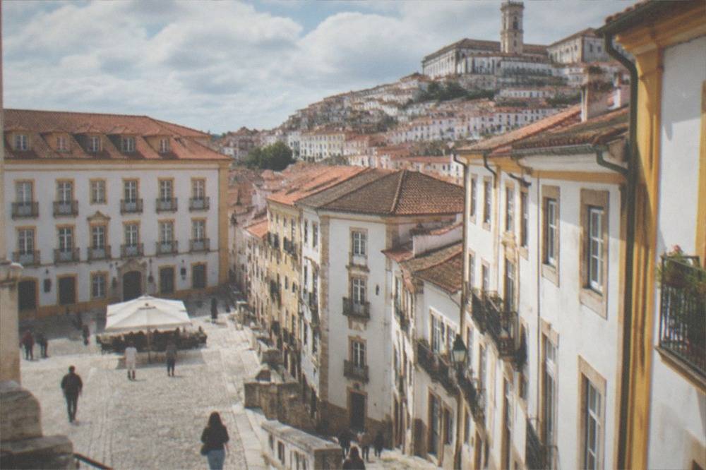 A cobbled square in central Coimbra with old buildings and people walking