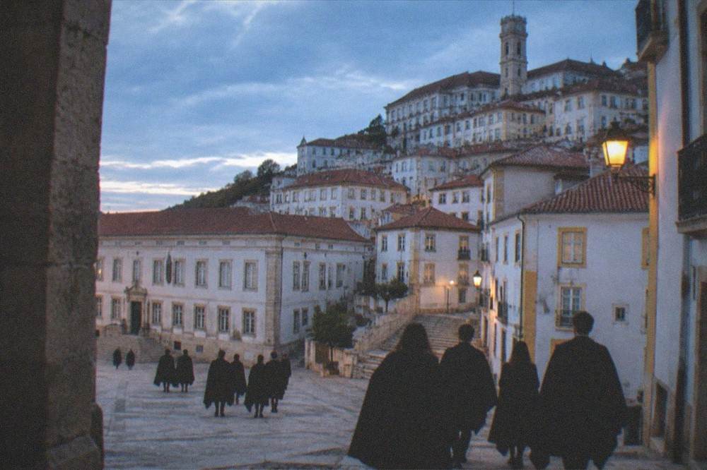 Students in traditional black capes walking through a square in Coimbra near the university.