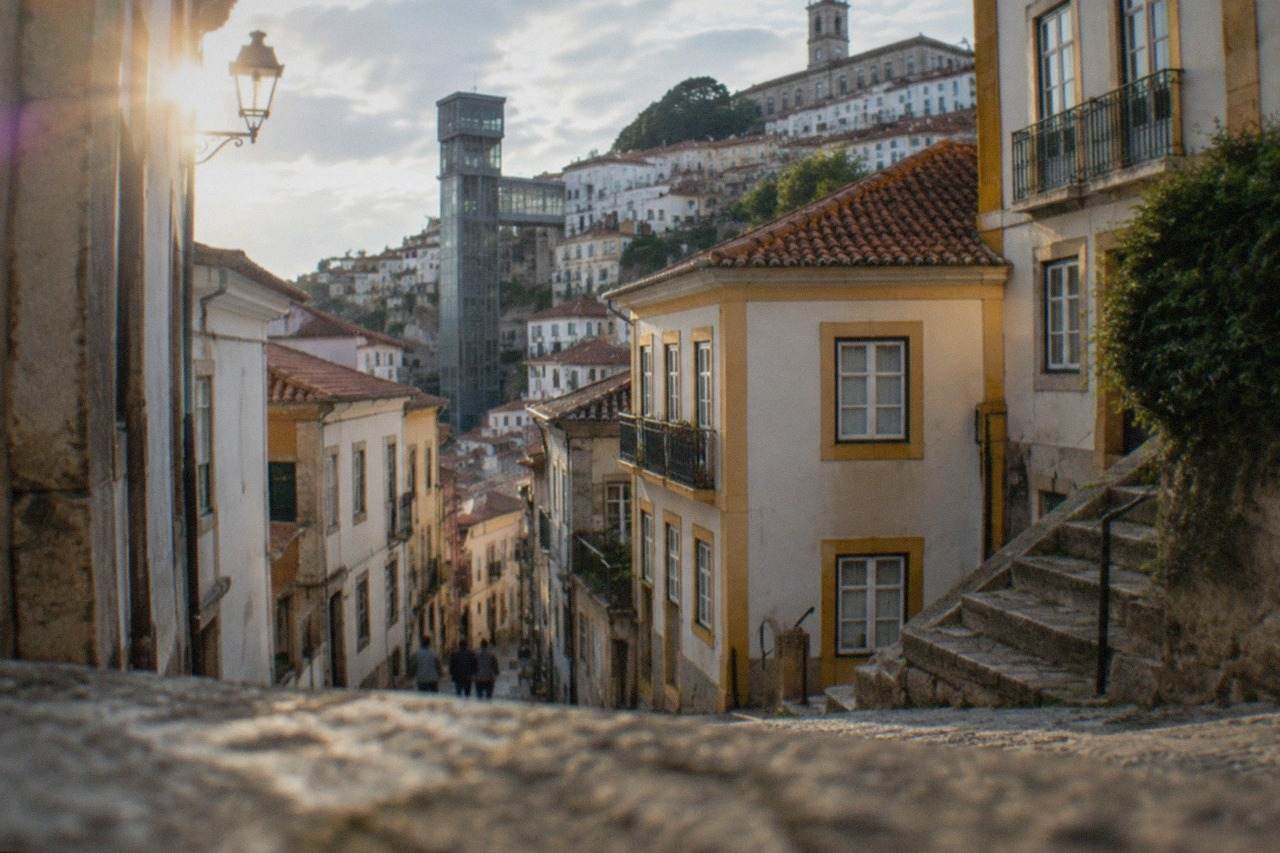 A public lift tower rising between the low streets of Coimbra and the hillside above them