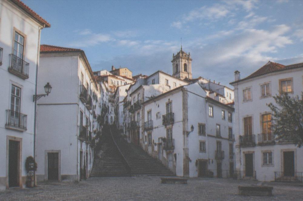 An empty cobbled square in Coimbra's upper town at dusk with warm light in the windows above
