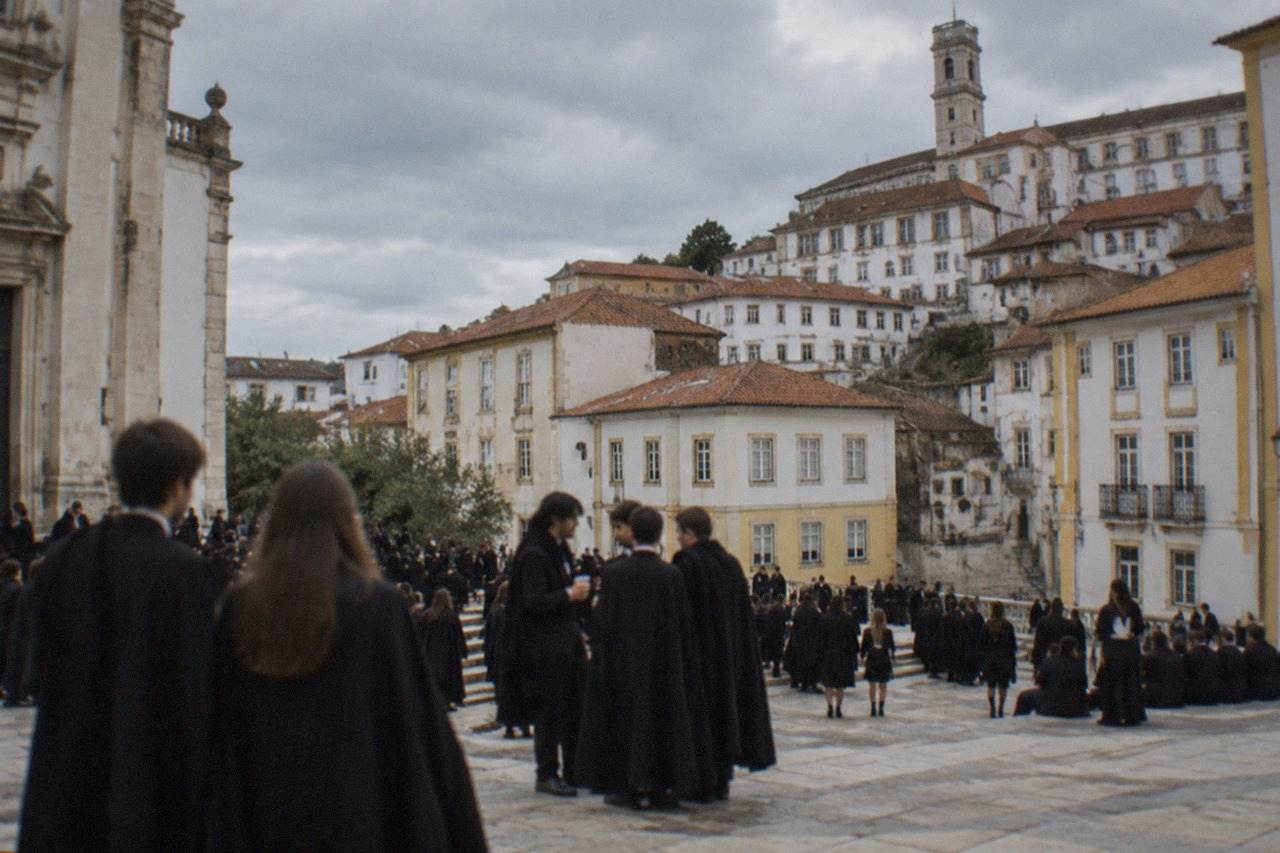 Crowds of students in black capes celebrating in a sunlit square of an old Portuguese university city