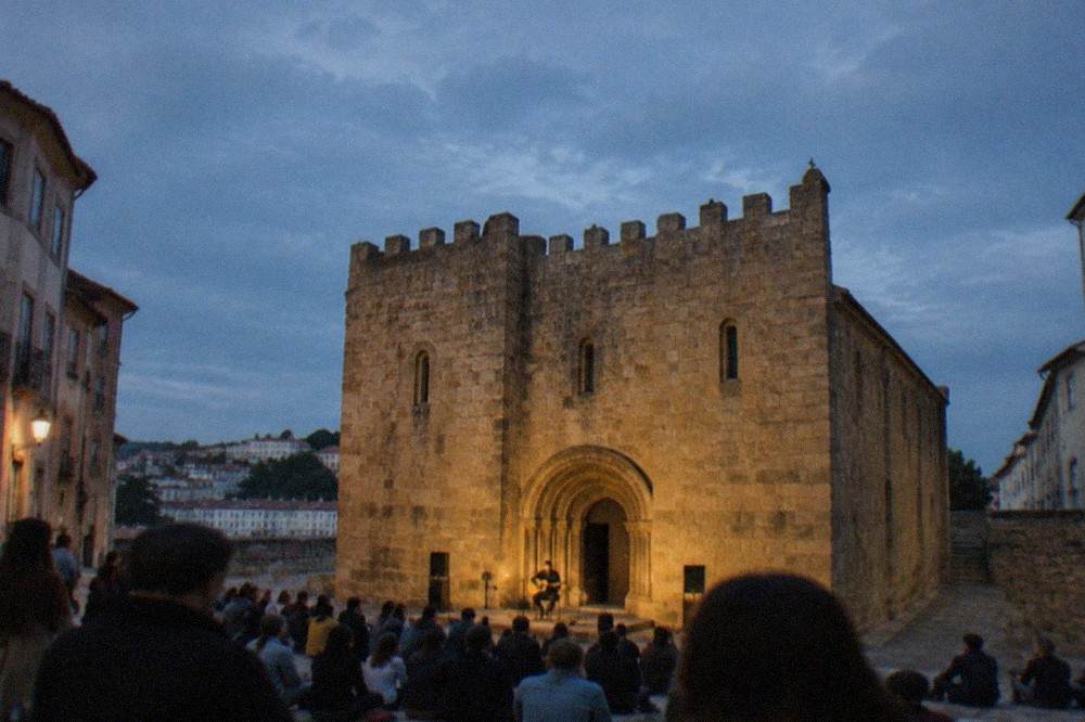 A night crowd gathered outside an old cathedral listening to a singer with a guitar