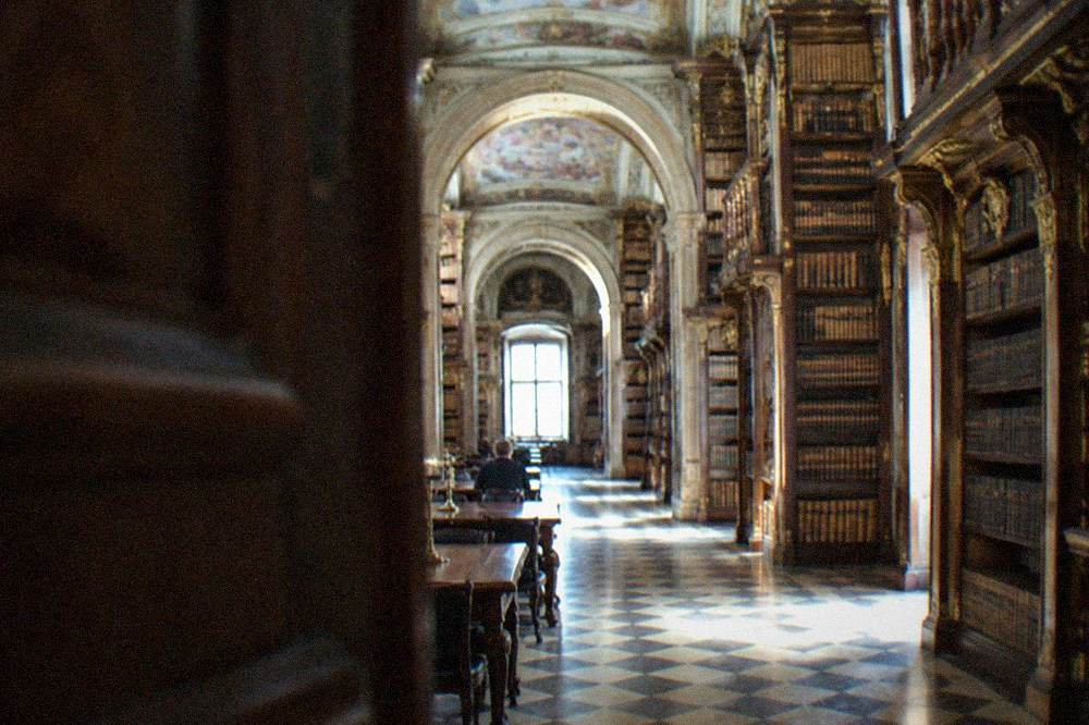 A baroque library hall with tall bookshelves and painted ceilings seen from the entrance