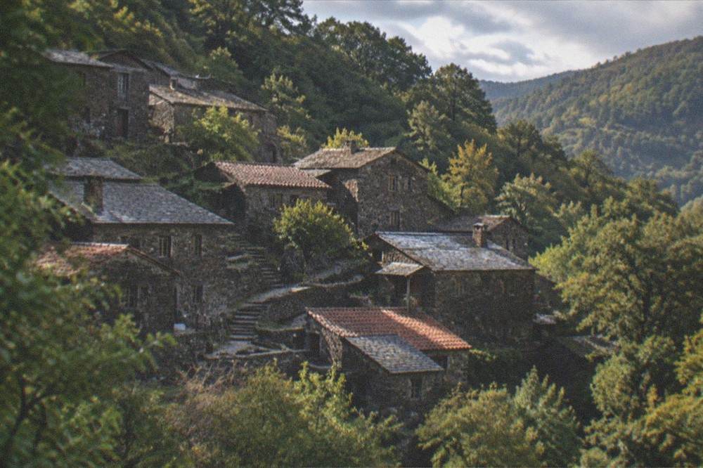 Stone houses with slate roofs on a forested mountainside in a Portuguese schist village