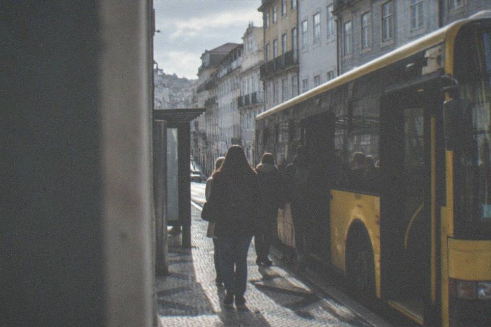 Passengers boarding a yellow city bus at a stop near Coimbra's downtown