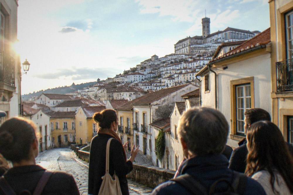 A small group on a free walking tour listening to a guide in a narrow old-town street of Coimbra