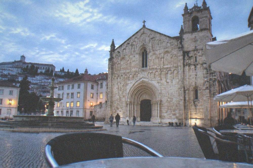 Café terrace with chairs on a cobbled square beside a stone monastery façade
