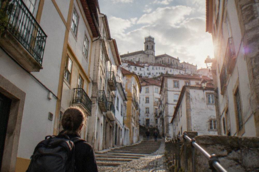 Traveller with a backpack looking up at a steep cobbled street lined with old buildings in Coimbra