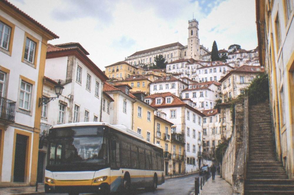 A city bus on a Coimbra street with the old town rising behind it