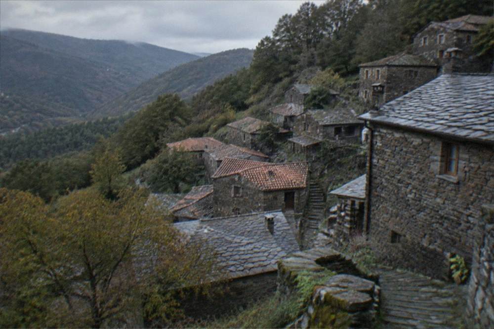 A hillside schist village with slate-roofed stone houses among trees above a valley